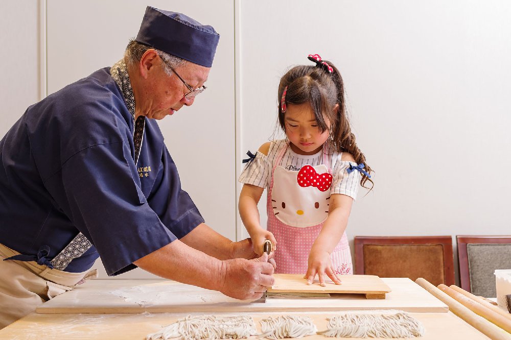 薄くのばしたそば団子を包丁で切る女の子の写真