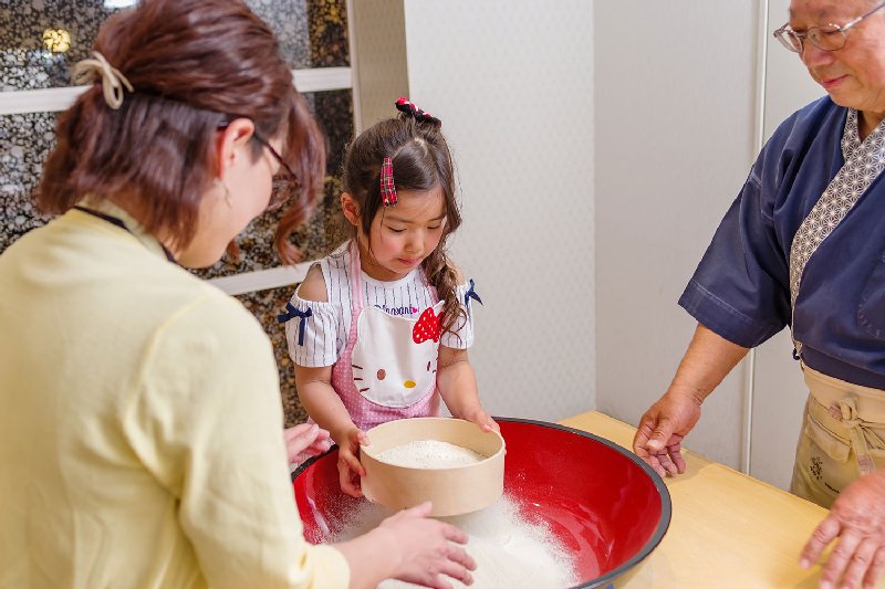そば粉を大きな器の中にふるい入れる女の子の写真