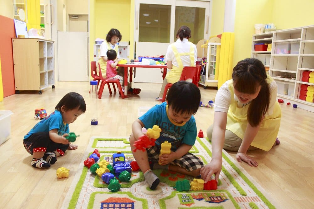 託児所内で遊ぶ保育士と乳幼児たちの写真
