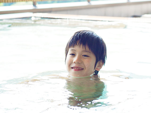 エンゼルグランディア越後中里の温泉大浴場の湯船に笑顔で入る男の子