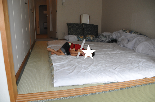 エンゼルグランディア越後中里　和室スタンダードの畳部分に、白い布団を3組敷いた上に寝転がる男の子の写真