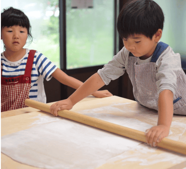 たくみの里　そば打ち体験で綿棒で生地を伸ばしている男の子の写真