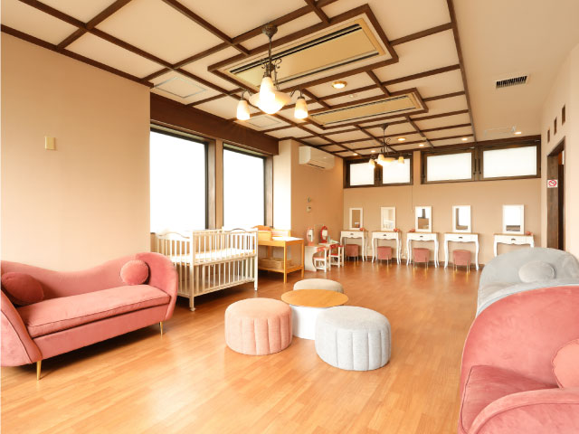 女性パウダールームにベビーベッド・オムツ替え台、ピンクのソファー、白い鏡台が5つ並んだ写真