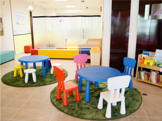 カラフルな色の子ども用チェアが、青くて丸いテーブルの周りに用意されたキッズコーナー